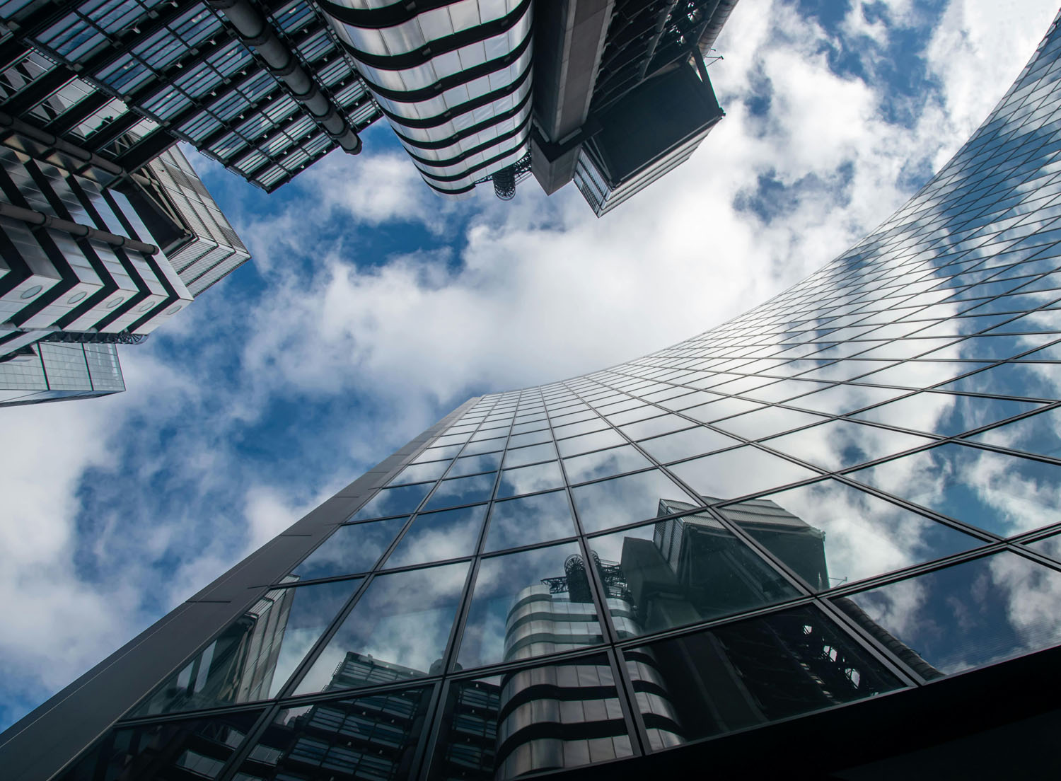 This is an image looking up to the sky with some office buildings and reflections of the opposite buildings in the glass.